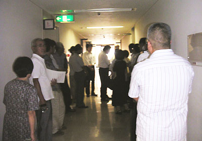 �L�҉���̑O�ő҂�